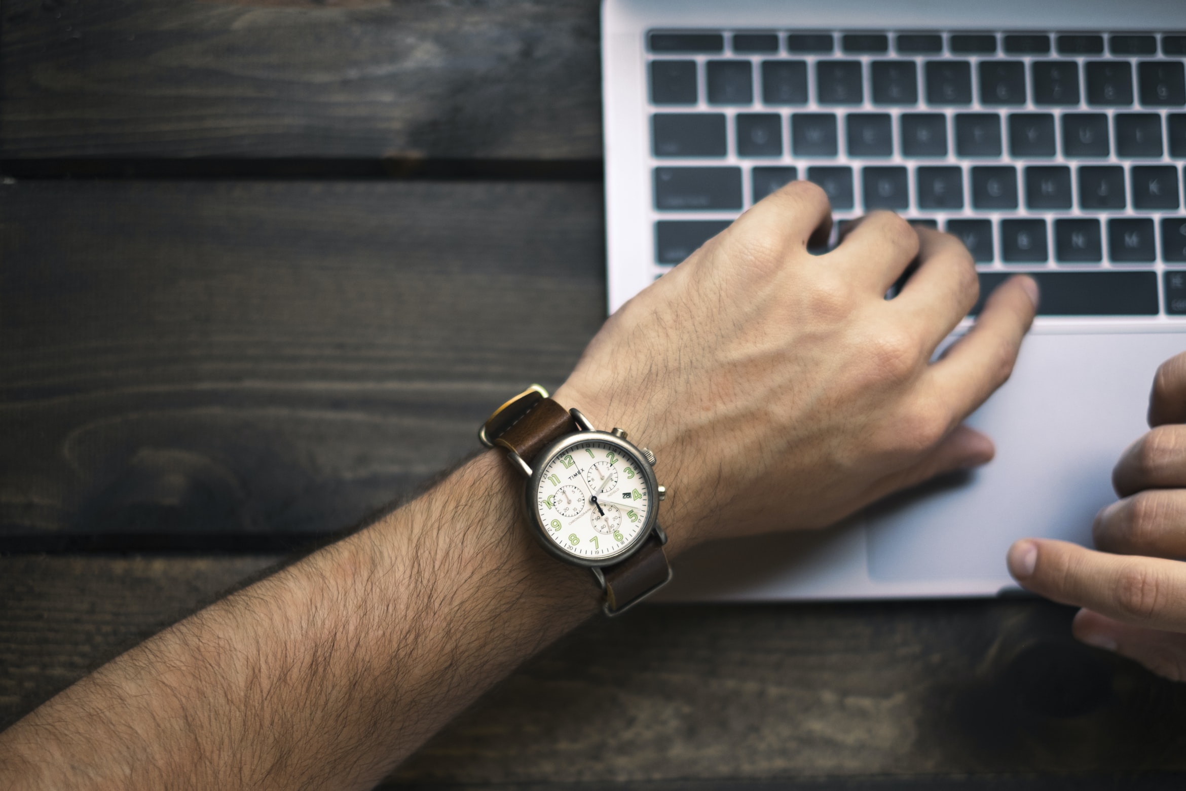 person wearing a brown watch while typing on his laptop