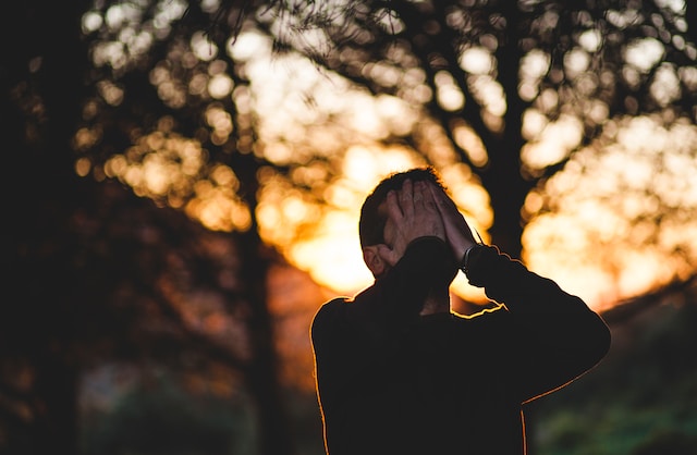 man wearing a black long sleeved shirt with his hands in his face